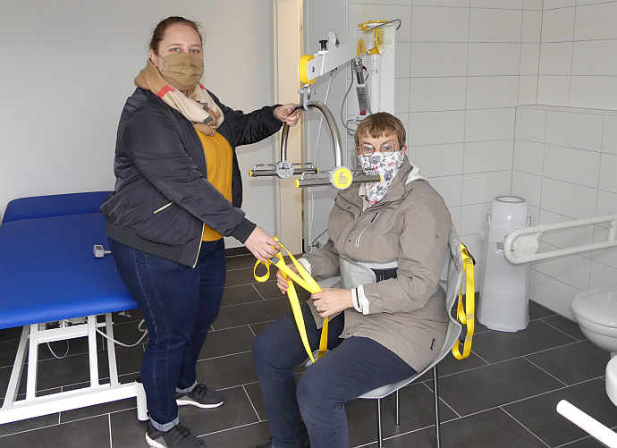 Jutta Pagel-Steidl und Nina Stockinger (beide LVKM) zeigen das Besondere einer »Toilette für alle«. Zunächst wird das Hebetuch angelegt und die Schlaufen am Patientenlifter eingehängt...<br />Foto: © Mara Sander