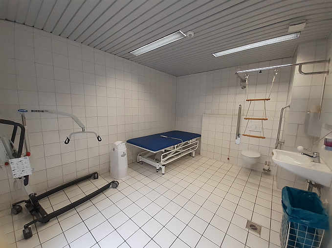 Die rund 12 qm große „Toilette für alle“  ist ausgestattet mit einer höhenverstellbaren frei stehenden Pfliege, einem mobilen Patientenlifter sowie einem luftdicht verschließbaren Windeleimer.