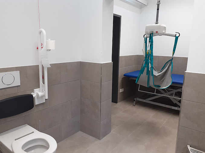 Die „Toilette für alle“  ist zusätzlich ausgestattet mit einer frei stehenden höhenverstellbaren Pflegeliege, Deckenlifter und luftdicht verschließbarem Windeleimer.