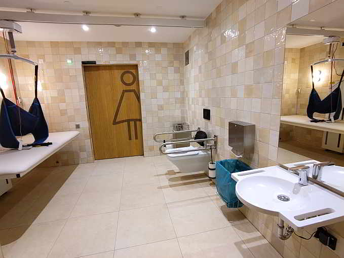 Die rund 13 qm große Rollstuhl-Toilette ist zusätzlich ausgestattet mit einer höhenverstellbaren Wandklappliege für Erwachsene, einem Deckenlifter (Hebetuch vorhanden) sowie einem luftdichten Windeleimer. Der Zugang zur „Toilette für alle“ erfolgt wahlweise über die Damen- oder Herrentoiletten. Der Zugang ist mit Euro-Schlüssel täglich zwischen 7 und 20 Uhr möglich.